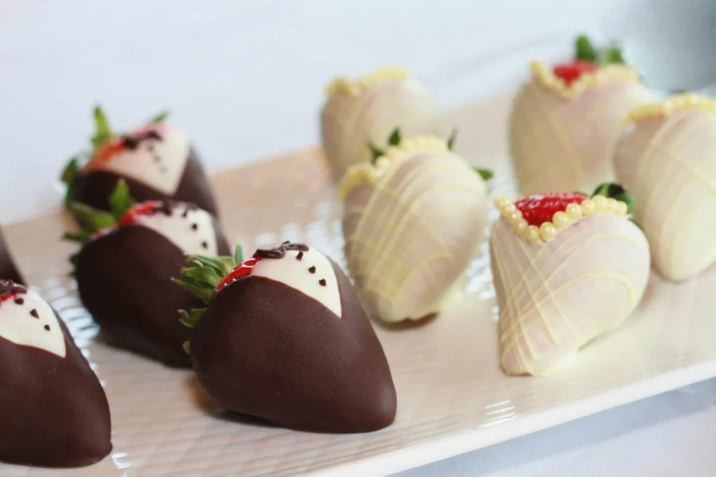 Artfully decorated chocolate-covered strawberries on a white rectangular platter.