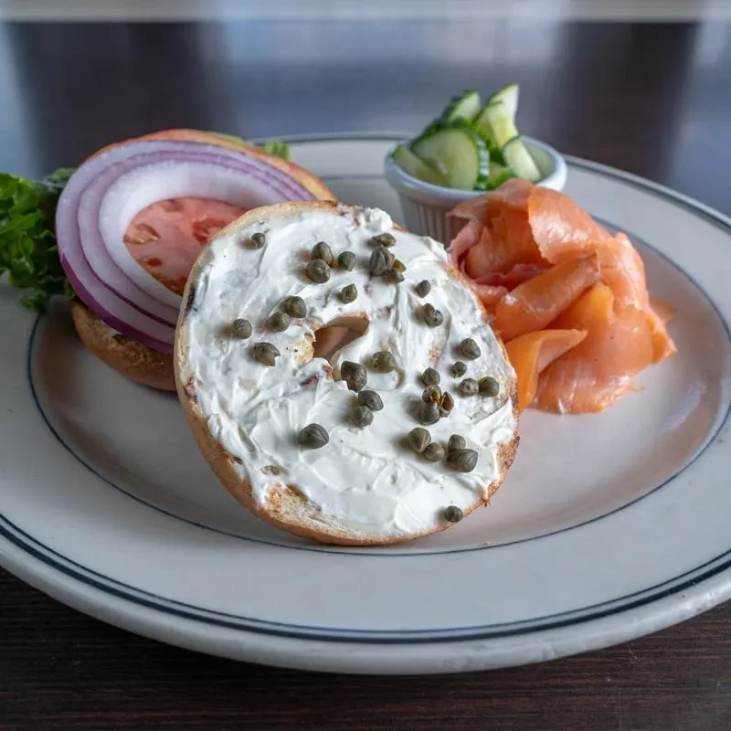 Bagel with lox, cream cheese, capers, and fresh vegetables on a plate.