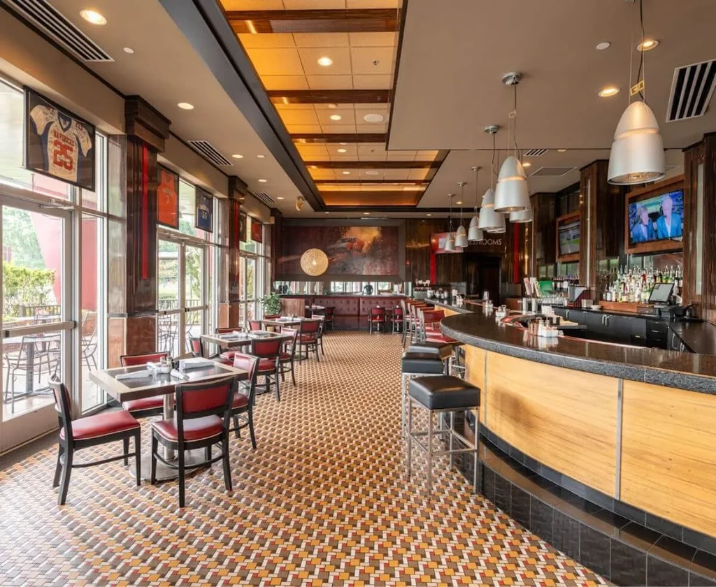 Spacious, well-lit restaurant and bar with red chairs, mosaic floor, and TVs.