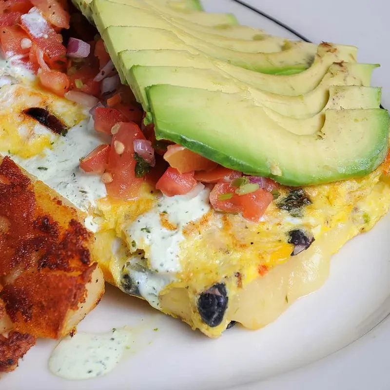 Omelet with pico de gallo, fanned avocado, creamy sauce, and roasted potatoes.