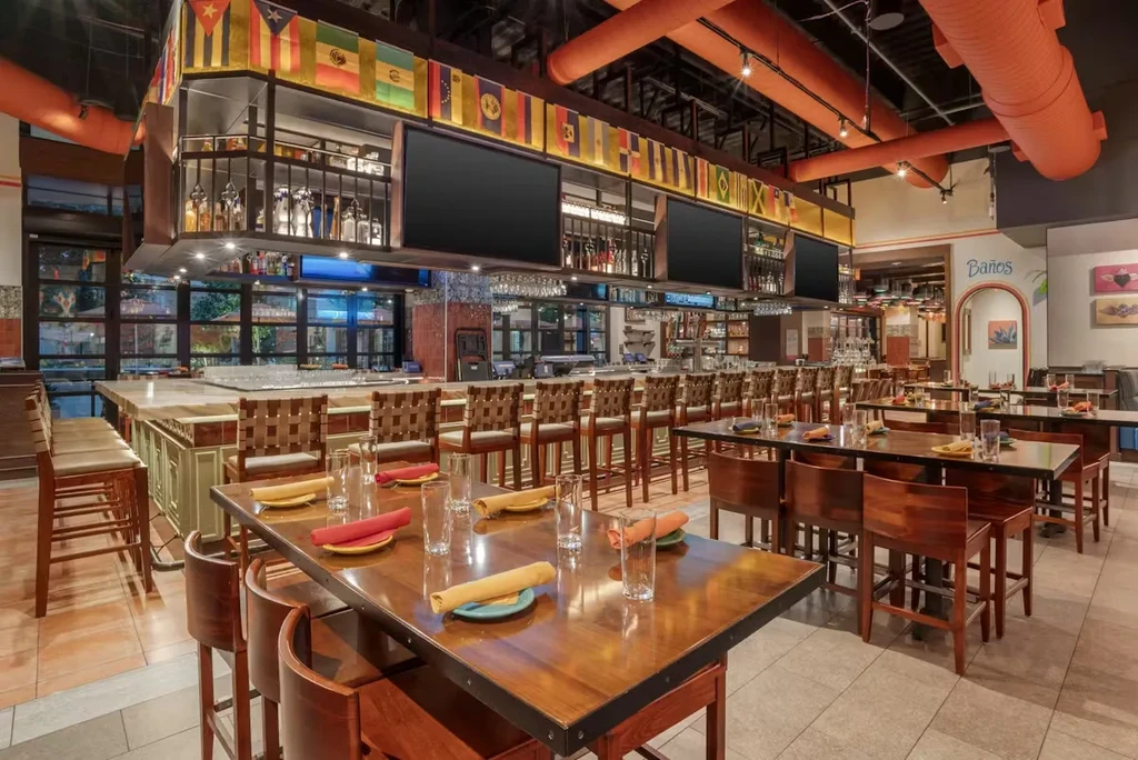 Empty vibrant restaurant interior with high-top tables, bar, Latin American flags.