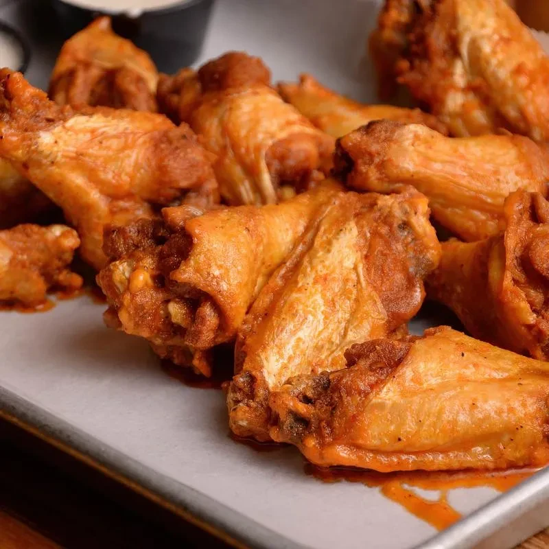 Saucy buffalo chicken wings on a tray with white dipping sauce.