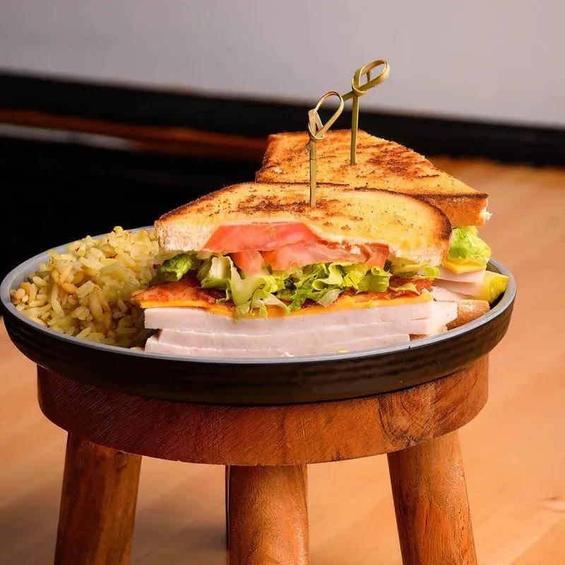Club sandwich, rice pilaf, and skewers on a rustic wooden stand.