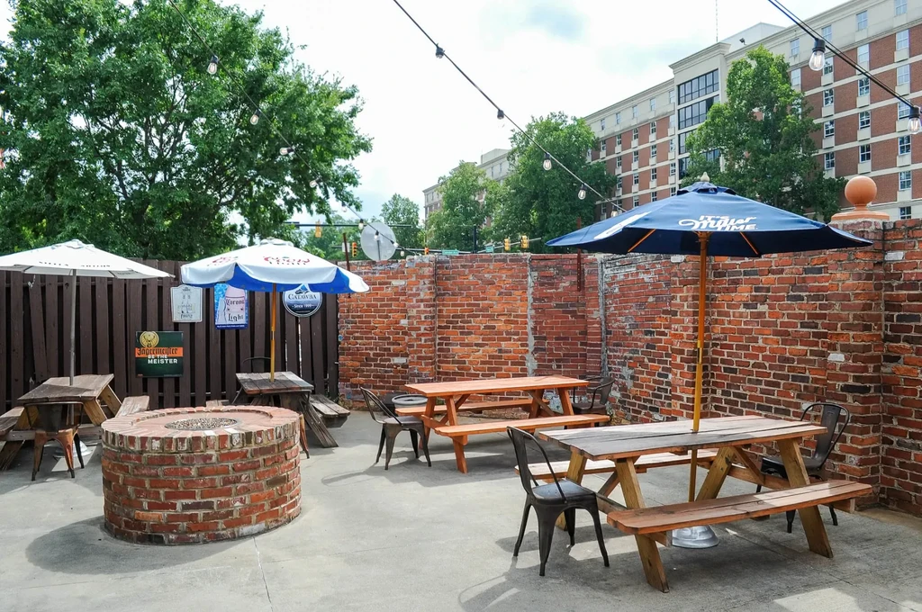 Empty outdoor patio with picnic tables, branded umbrellas, and string lights.