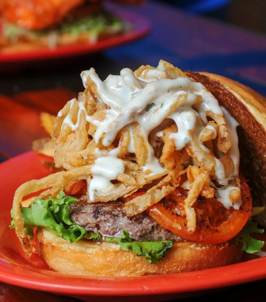 Close-up gourmet burger with crispy fried onions and creamy sauce.