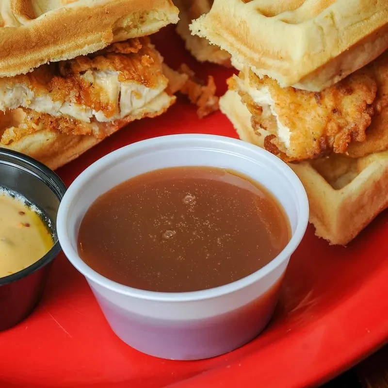 Close-up: crispy chicken and waffles with sauces on a red plate.