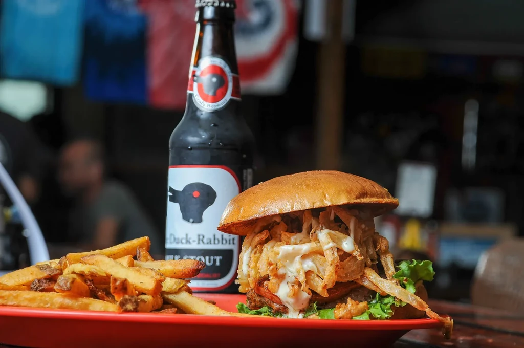 Burger, fries on red plate, beside chilled Duck-Rabbit Milk Stout beer.