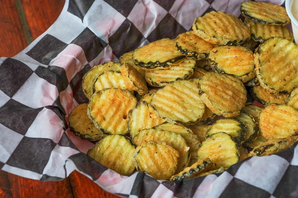 Overhead shot of crispy, golden-brown fried pickles in a checkered basket.