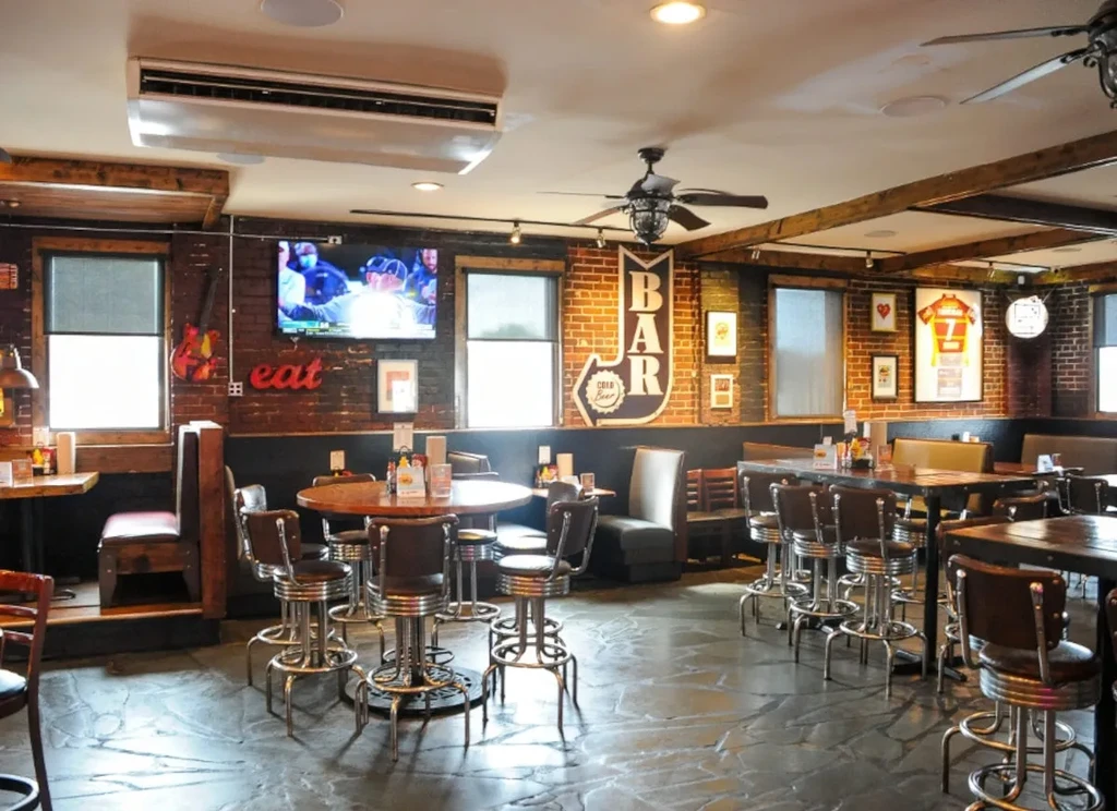 Rustic industrial restaurant interior with exposed brick, mixed seating, and bar sign.