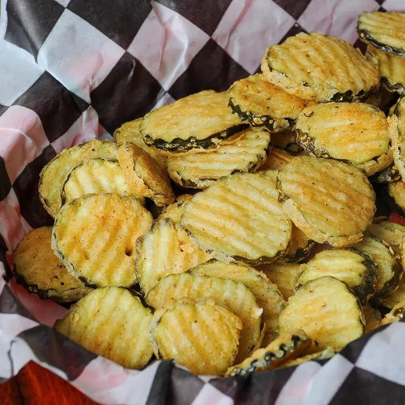 Crispy, golden-brown fried pickles in a checkered paper-lined basket.