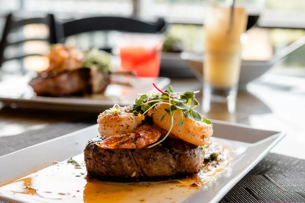 Grilled steak and seafood entree on a white plate in a restaurant.