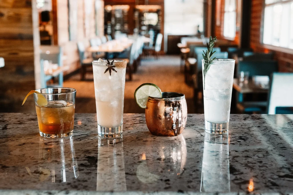 Four distinct cocktails with ice and garnishes on a bar countertop.