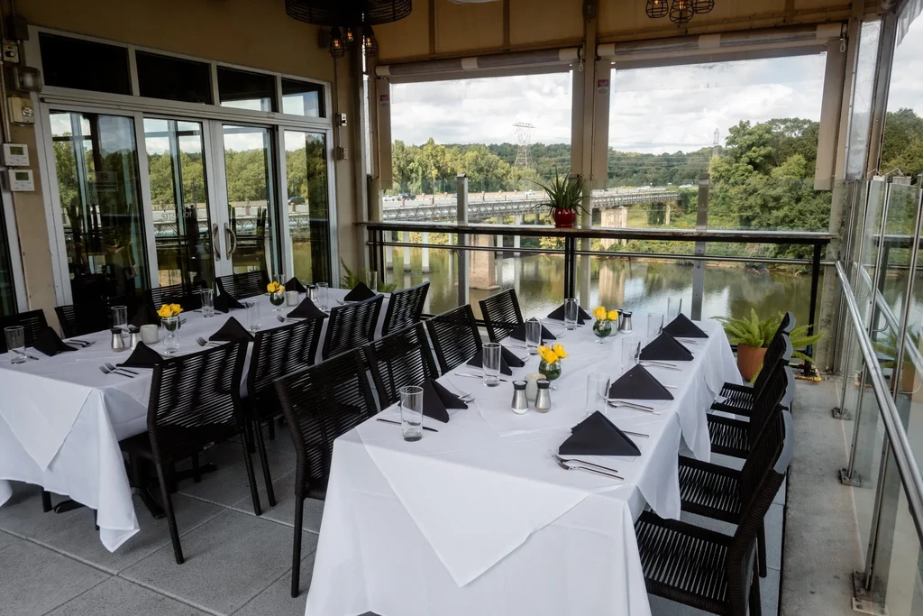 Elegant outdoor dining tables overlook a scenic river and bridge.