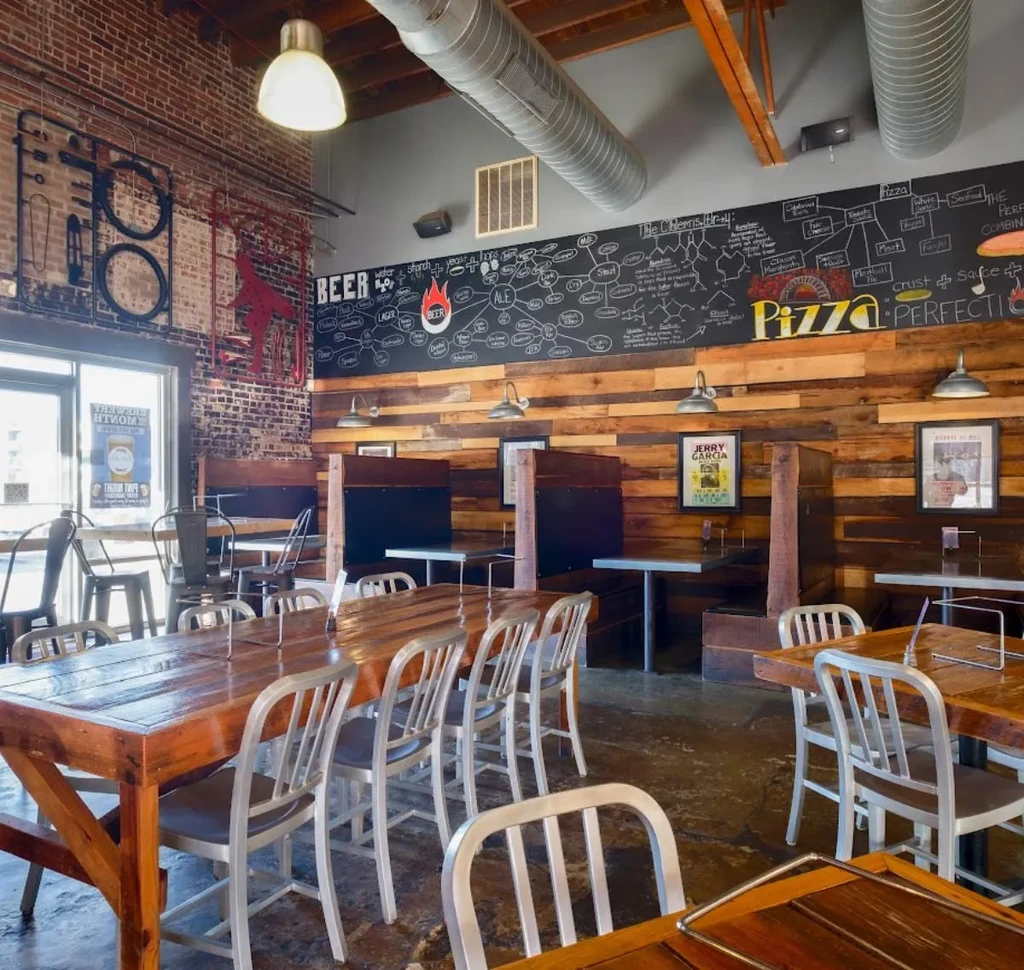 Rustic industrial restaurant with communal table, brick walls, and beer/pizza chalkboard.