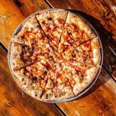 Sliced pizza with charred crust, meat, and cheese on wooden table.