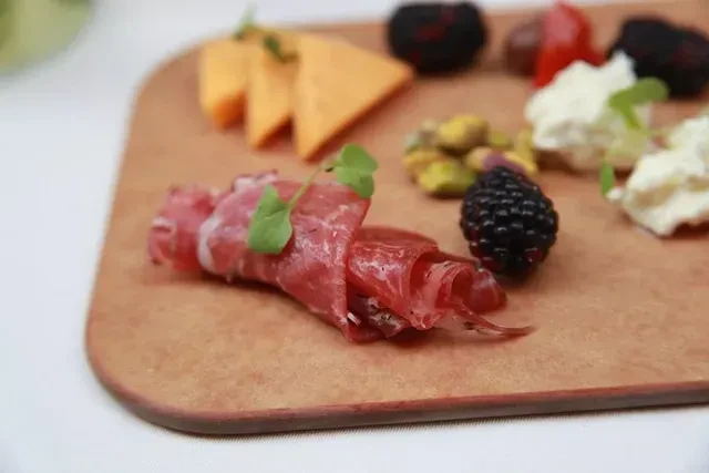Prosciutto roll, blackberry, cheddar, and pistachios on a wooden board.