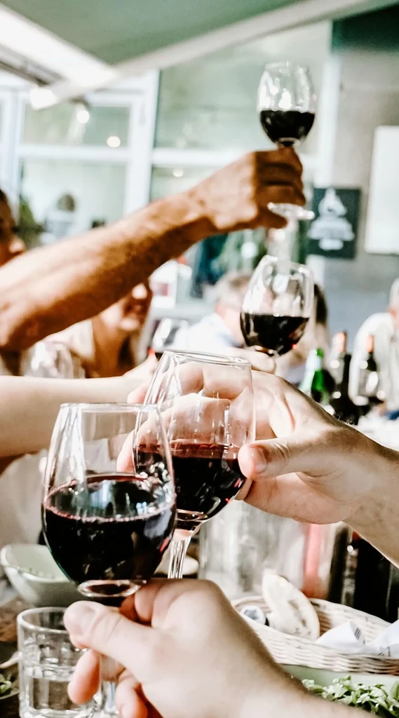 Multiple hands holding red wine glasses, toasting in a restaurant.
