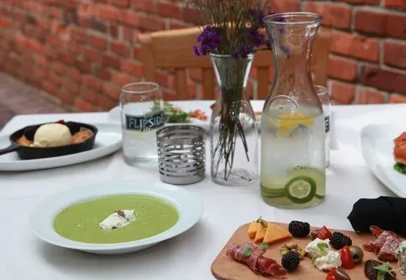 Well-set outdoor table with dessert, green soup, charcuterie, and infused water.