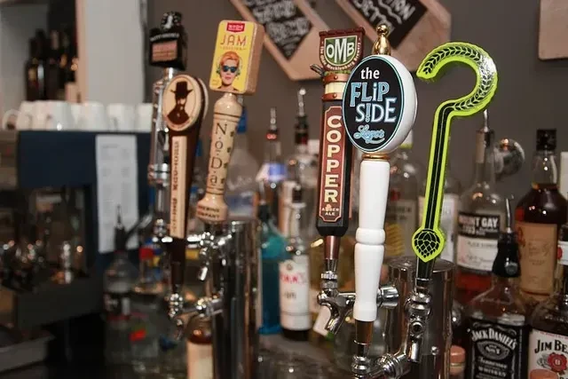 Five distinct beer tap handles with liquor bottles in the background.