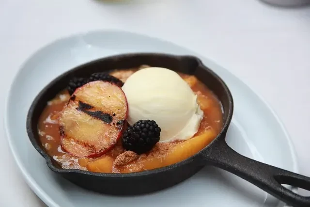 Skillet peach cobbler with grilled peaches, vanilla ice cream, and blackberries.