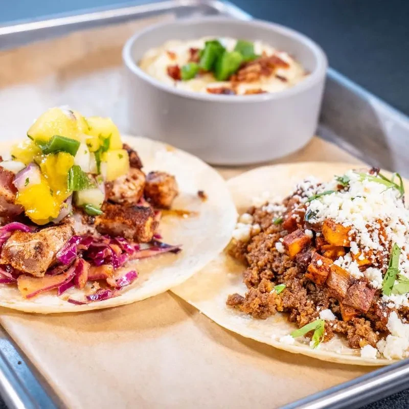 Two distinct tacos and a side dish on a parchment-lined tray.