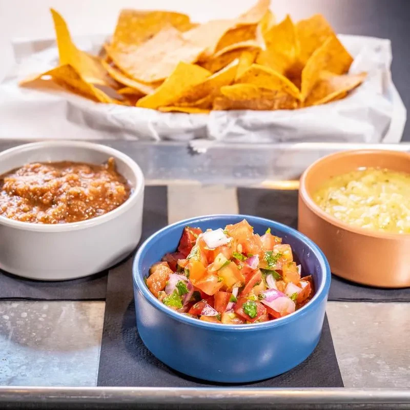 Close-up of nachos and three dips: salsa, pico de gallo, creamy dip.