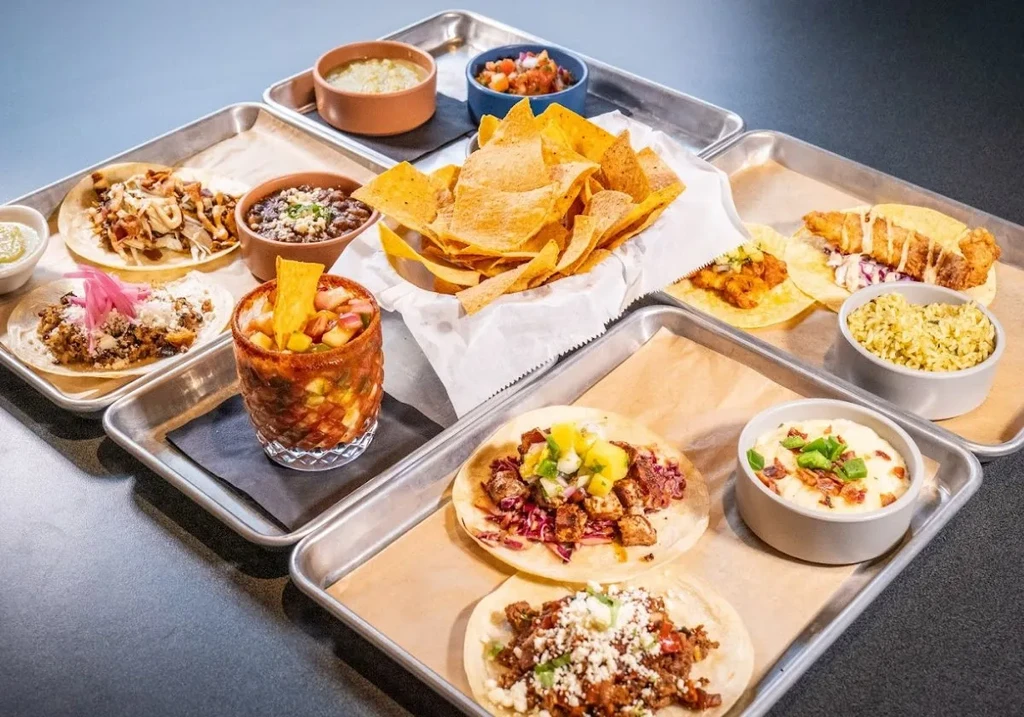 A vibrant array of Mexican tacos, chips, dips, rice, and a drink.