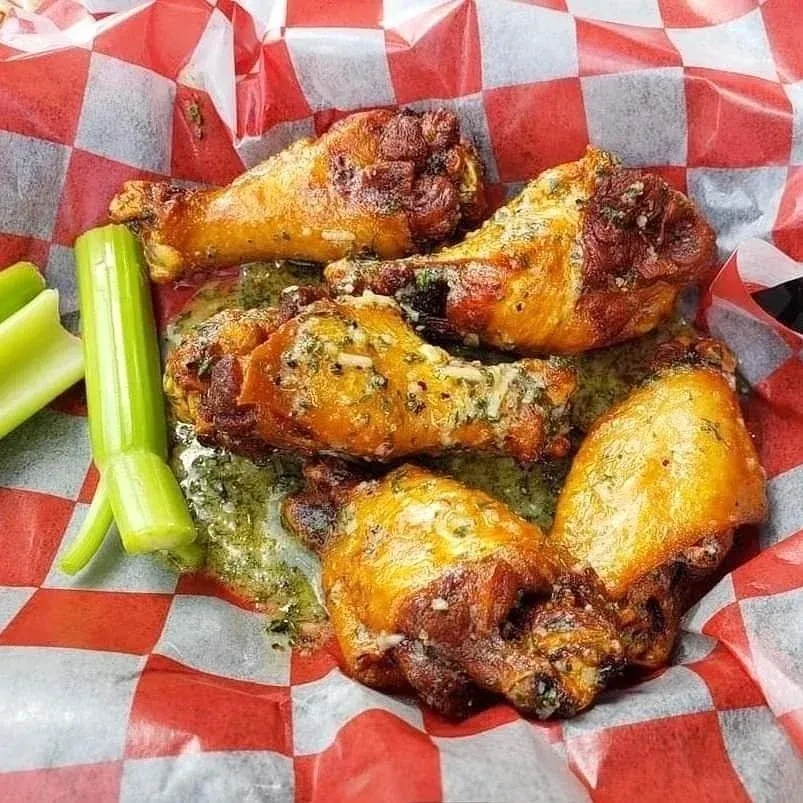 Five sauced chicken wings, celery, and green sauce in a checkered basket.