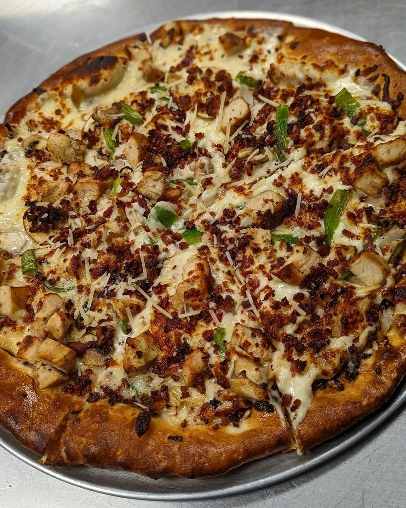 Freshly baked white sauce pizza with chicken, bacon, peppers, mushrooms.