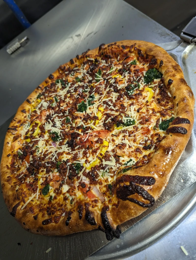 Well-baked pizza topped with cheese, bacon, tomatoes, spinach on metal.