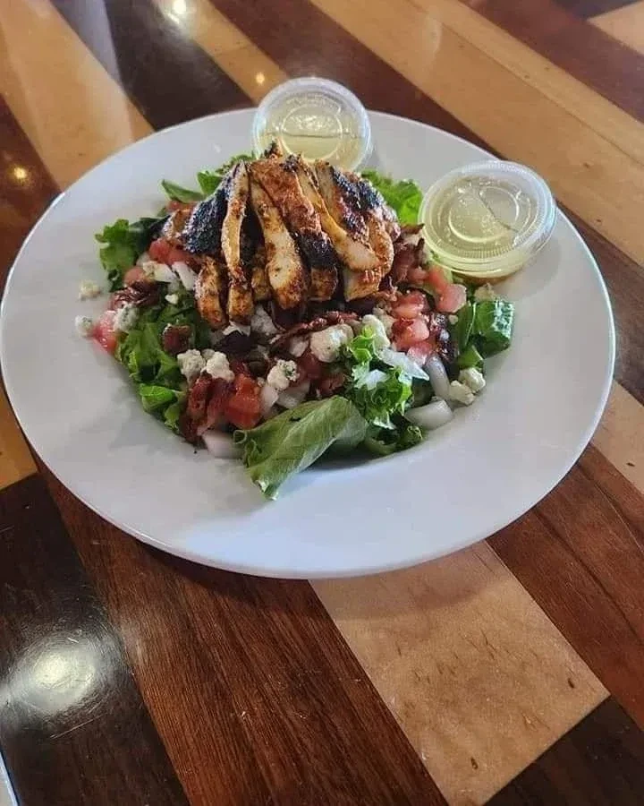 Grilled chicken salad, blue cheese, bacon, dressing on white plate.