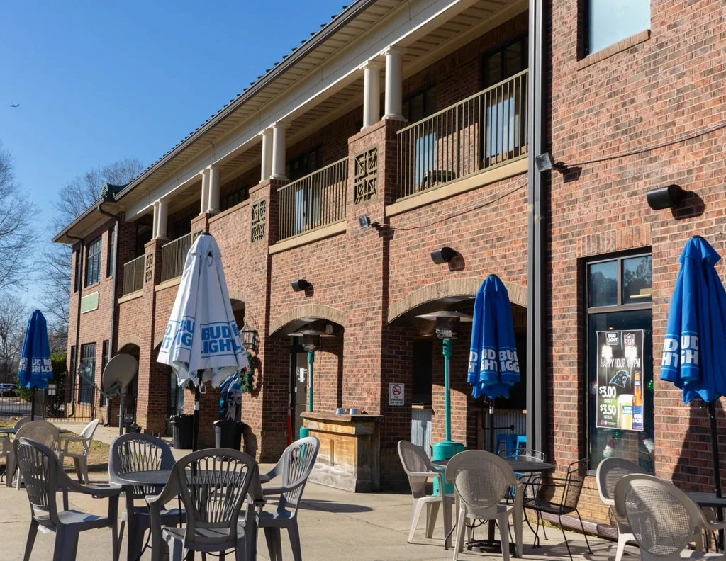 Brick restaurant building with patio, umbrellas, and happy hour sign.