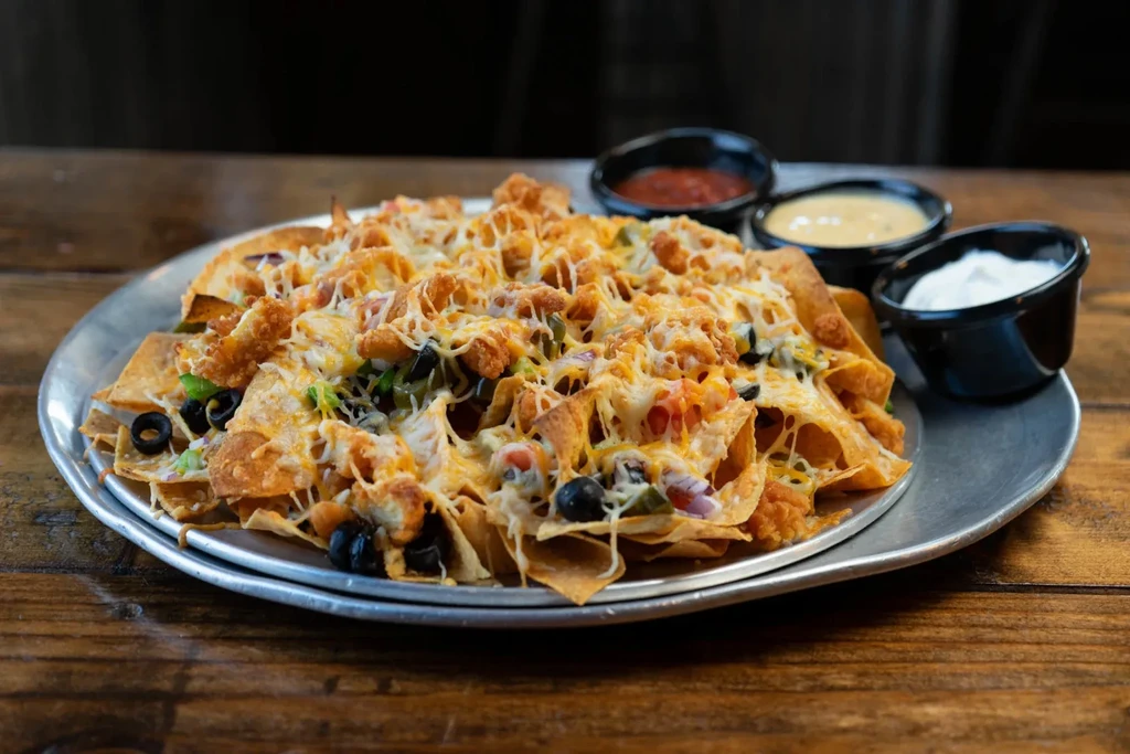 Fully loaded chicken nachos with cheese, vegetables, and three dips.