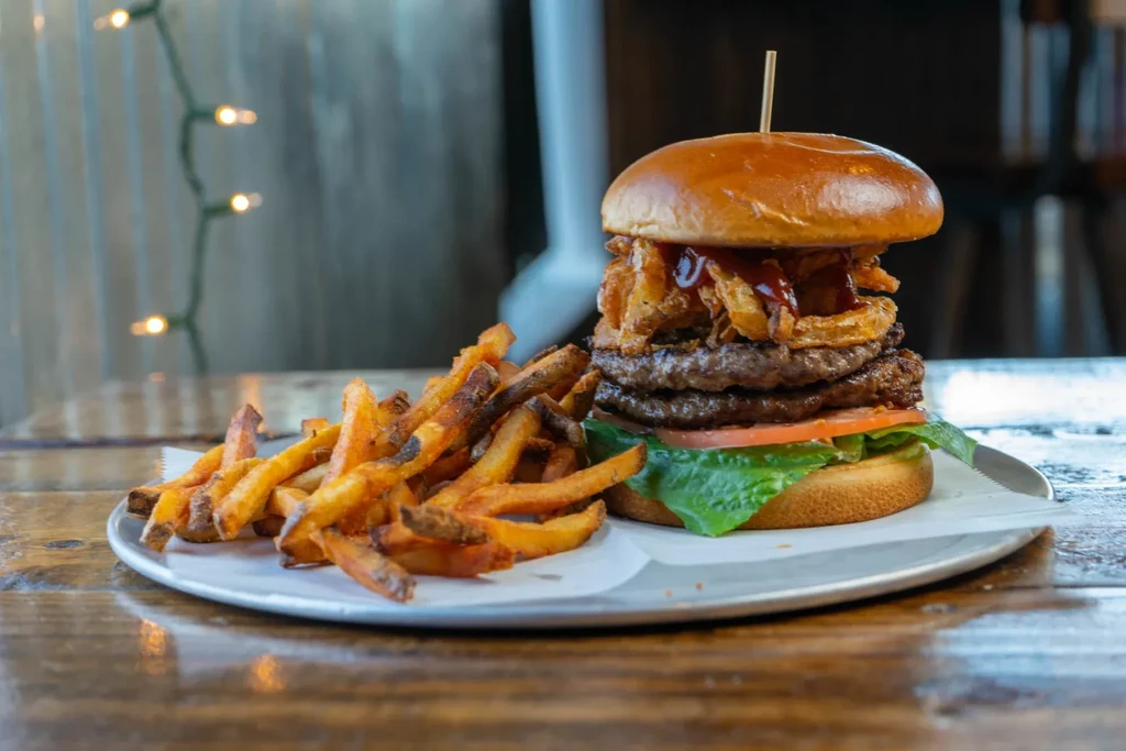 Large stacked burger with fried onions and crispy french fries.