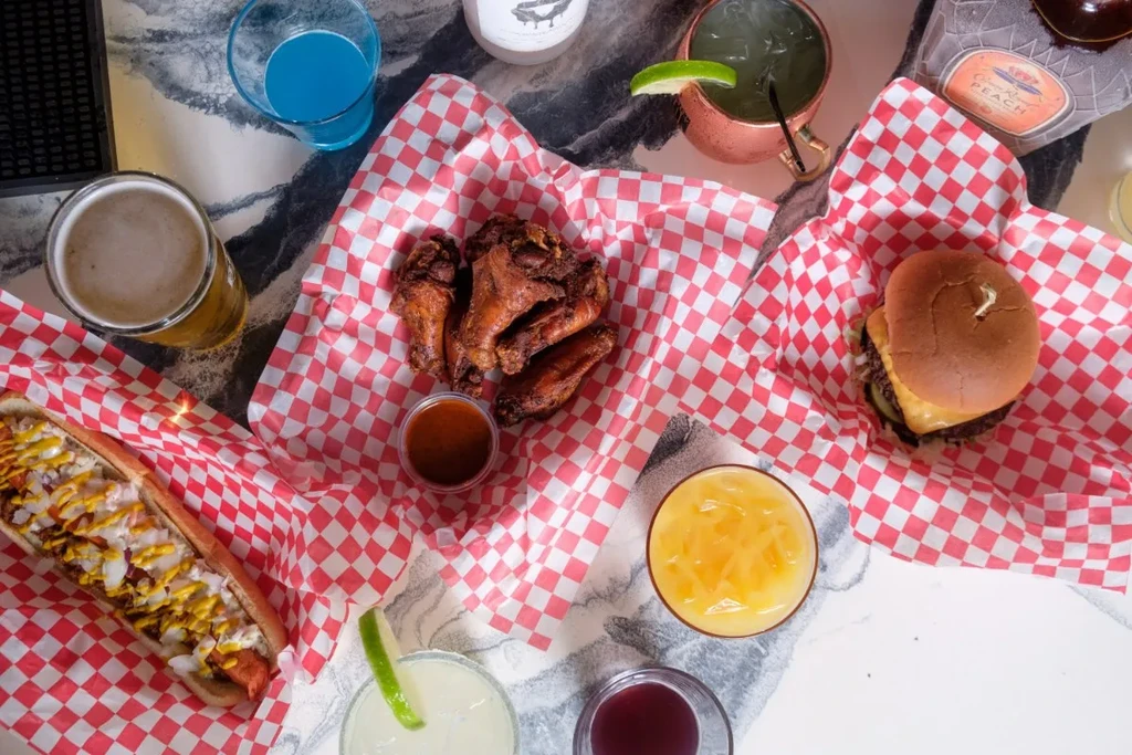Overhead table with hot dog, wings, cheeseburger, beer, and cocktails.