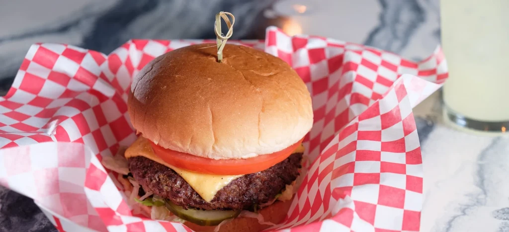 Cheeseburger with melted cheese, tomato, lettuce, and skewer on checkered paper.