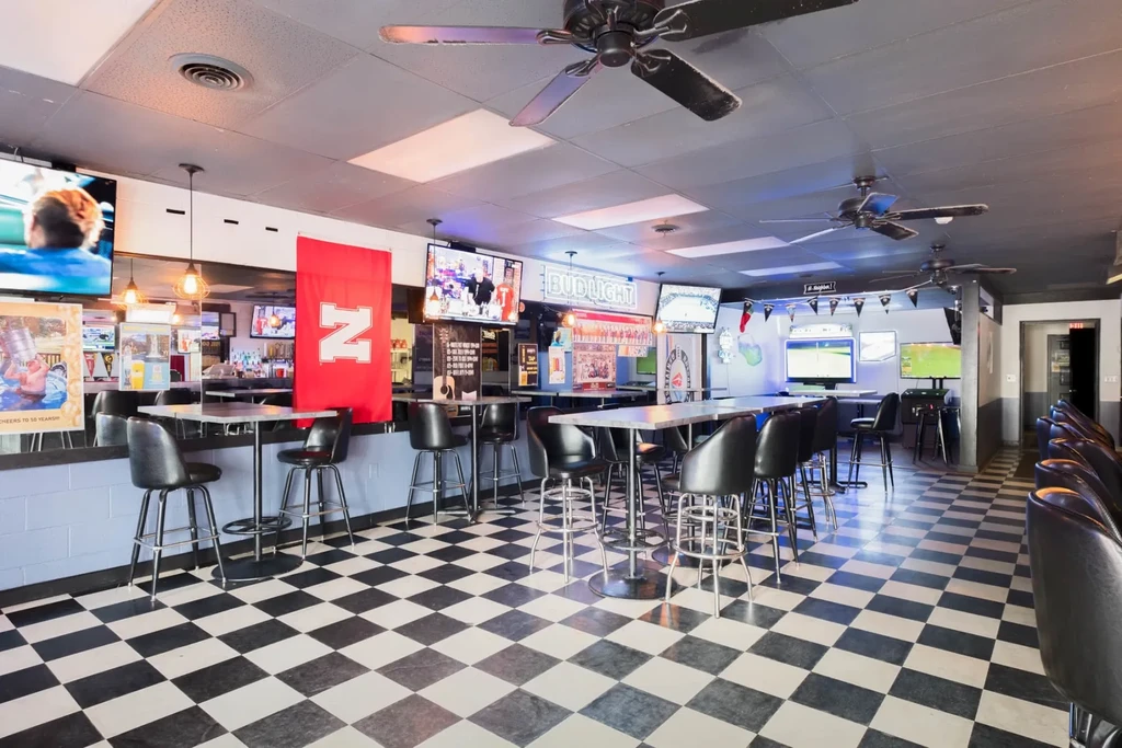 Empty sports bar interior with checkerboard floor, bar, and TVs.