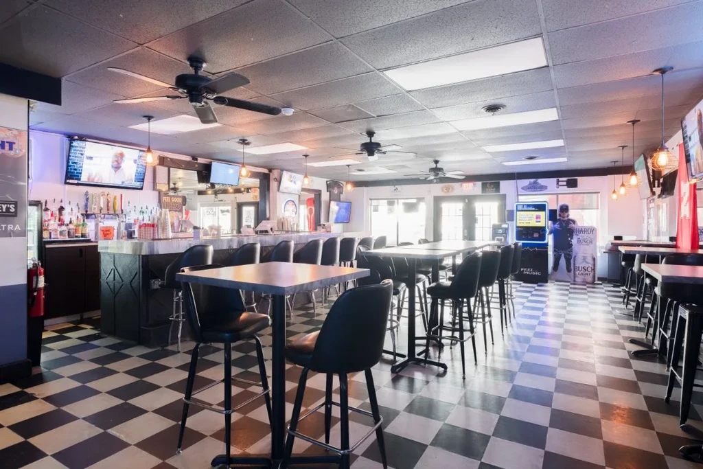 Empty casual bar with checkerboard floor, long bar, and high-top tables.