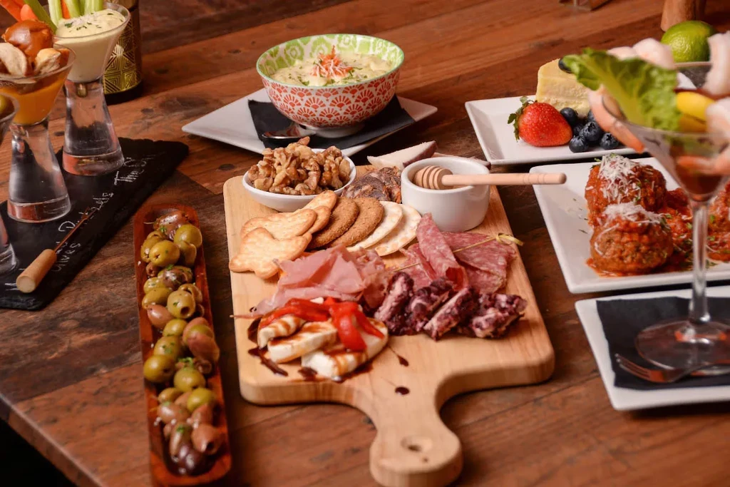 Rustic wooden table holds appetizers including charcuterie, olives, and meatballs.