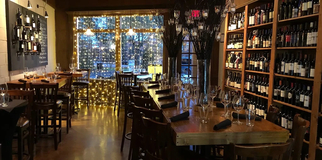 Warm restaurant interior with wooden tables, extensive wine selection, and fairy lights.