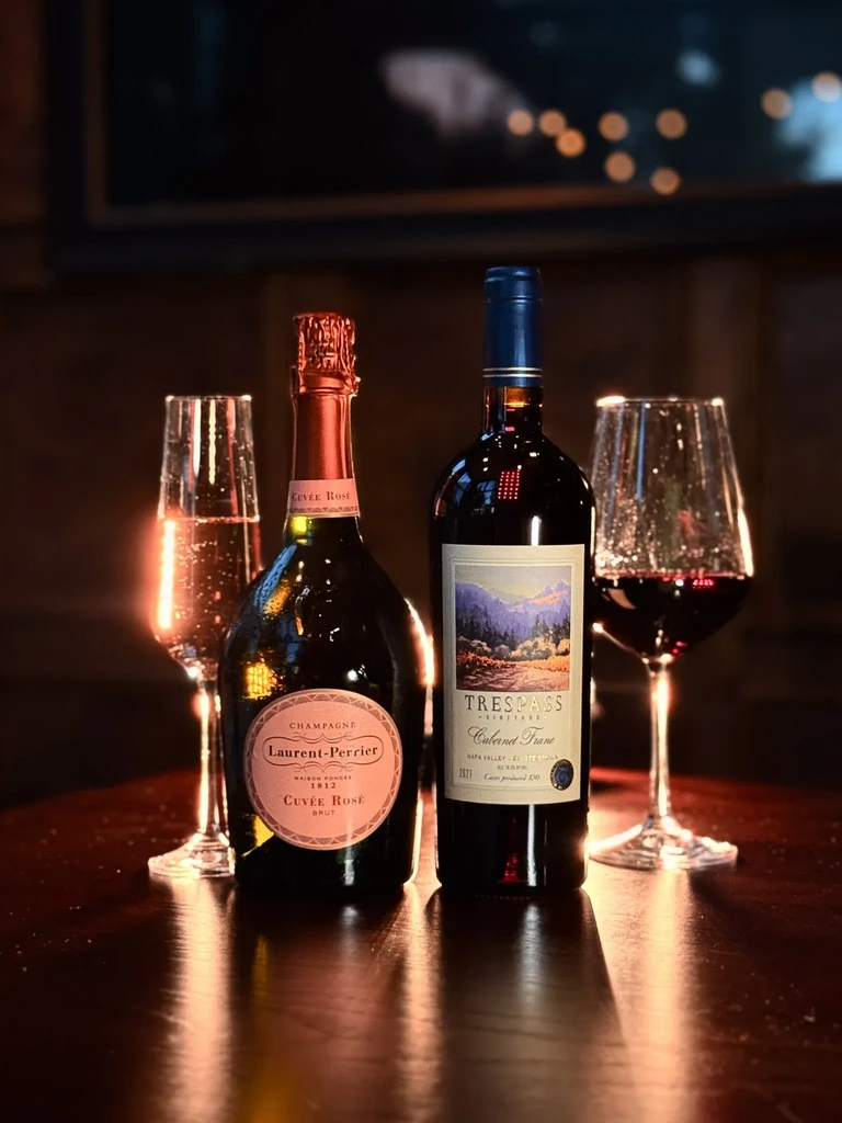 Champagne and red wine bottles with filled glasses on dark wood.