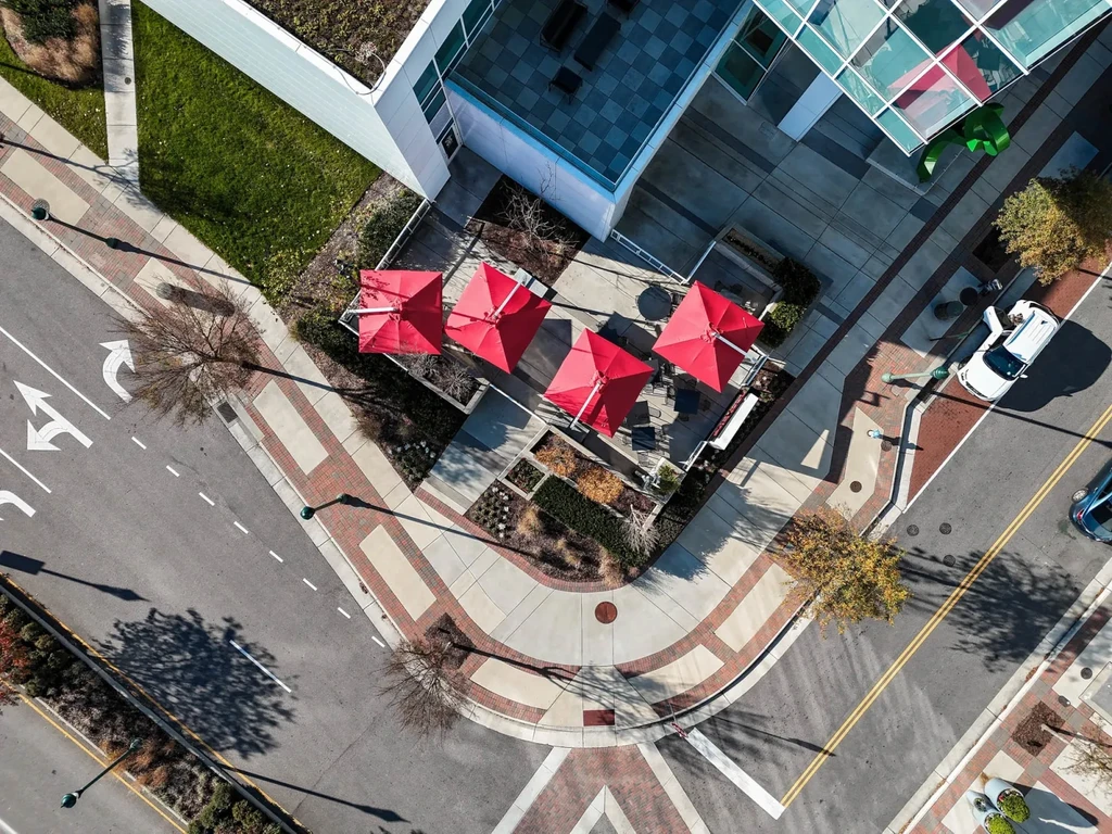Aerial view of a modern building with red umbrellas and green roof.