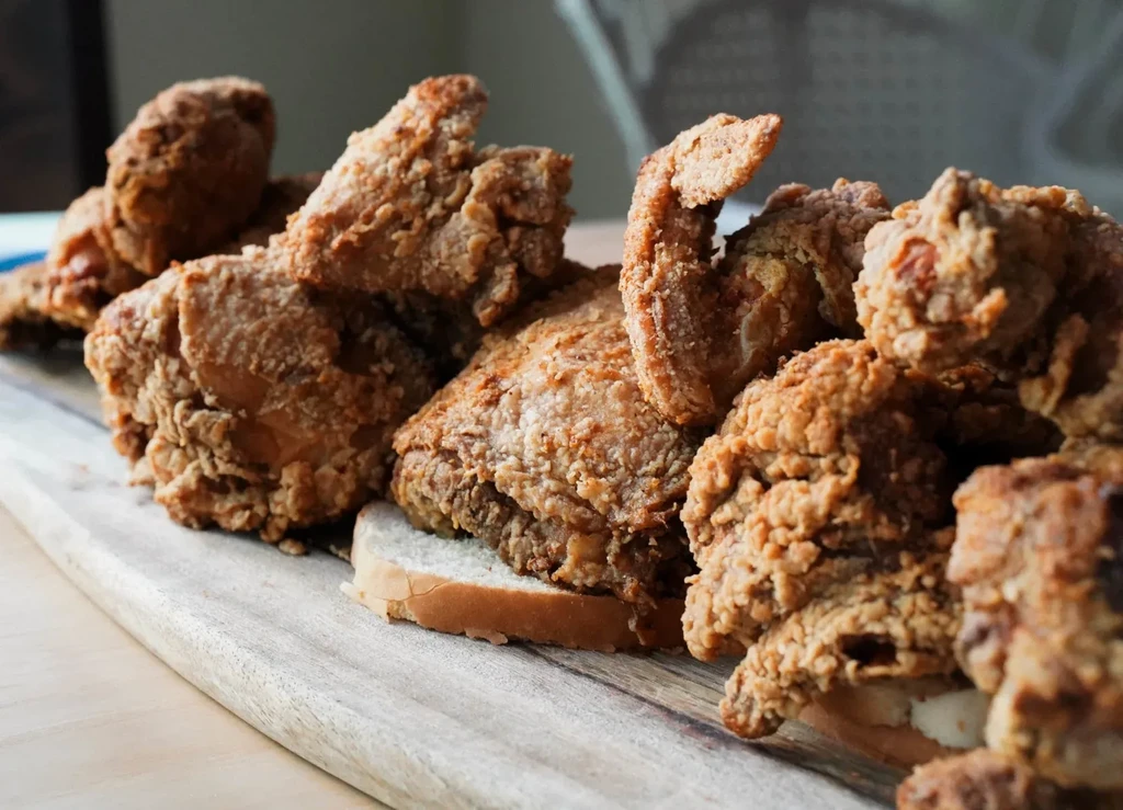 Golden-brown fried chicken with crispy crust on wood and white bread.