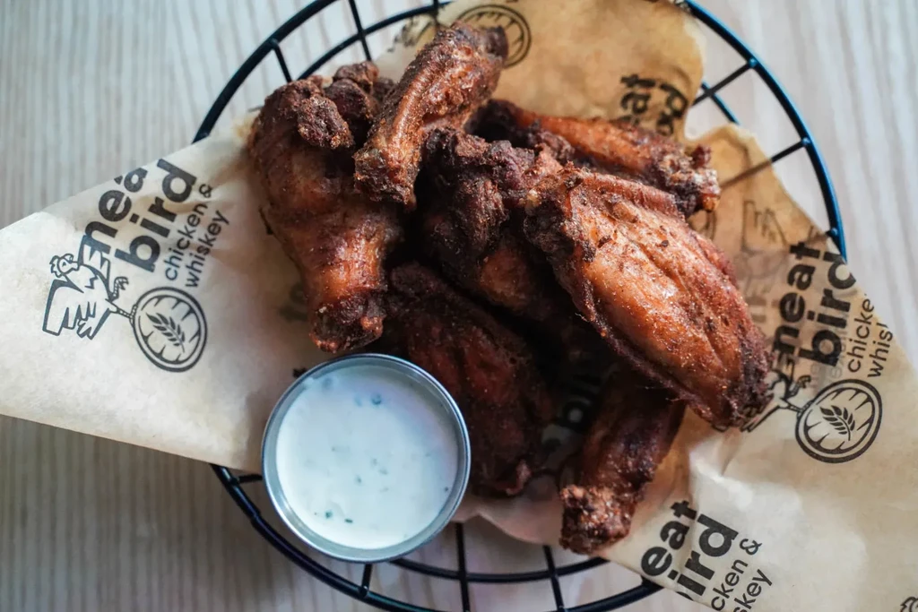 Crispy, seasoned chicken wings in black basket with creamy sauce.