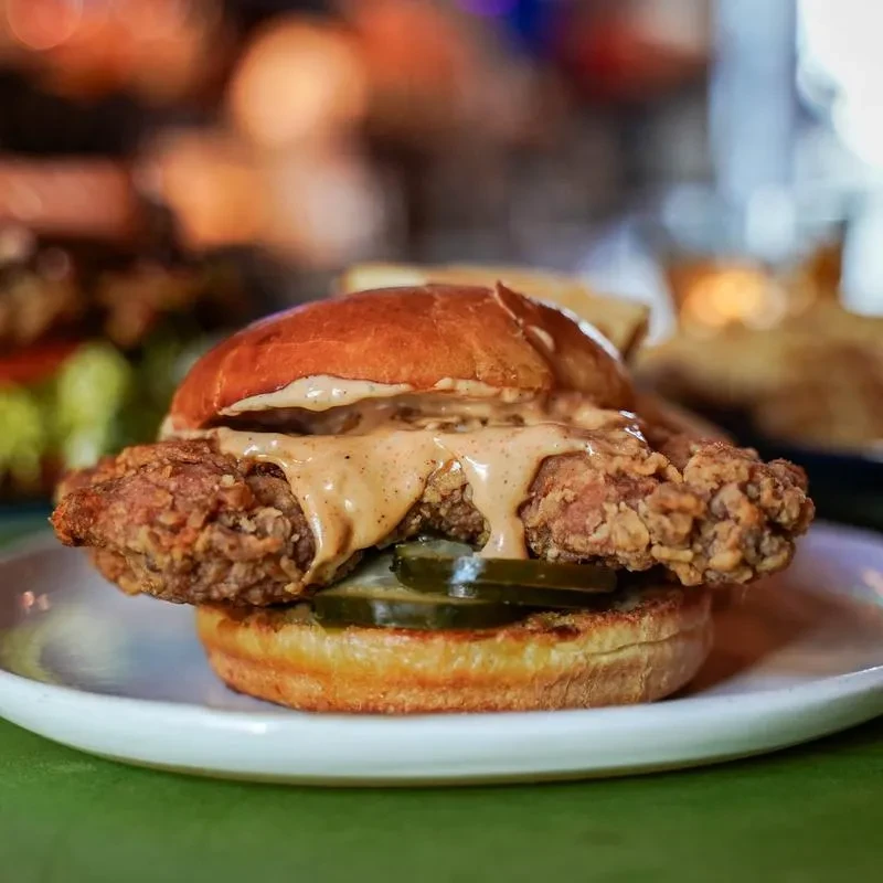 Close-up crispy fried chicken sandwich with pickles and sauce.
