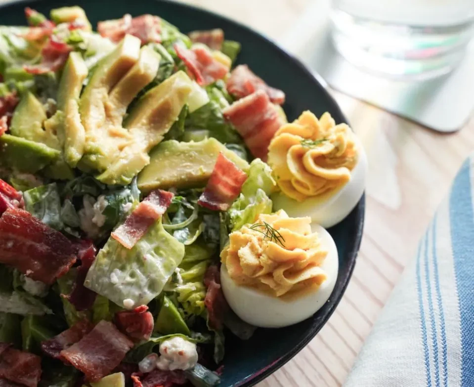 Hearty salad with bacon, avocado, cheese, and two deviled eggs.
