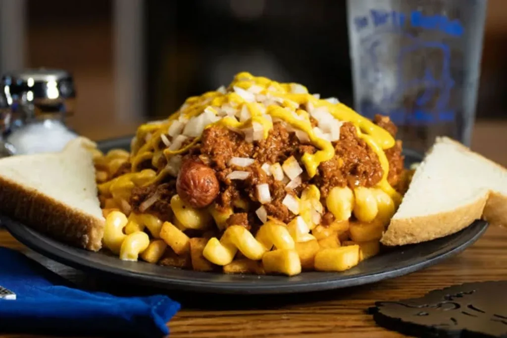 A hearty diner meal of fries, mac, chili, hot dogs, mustard, onions.