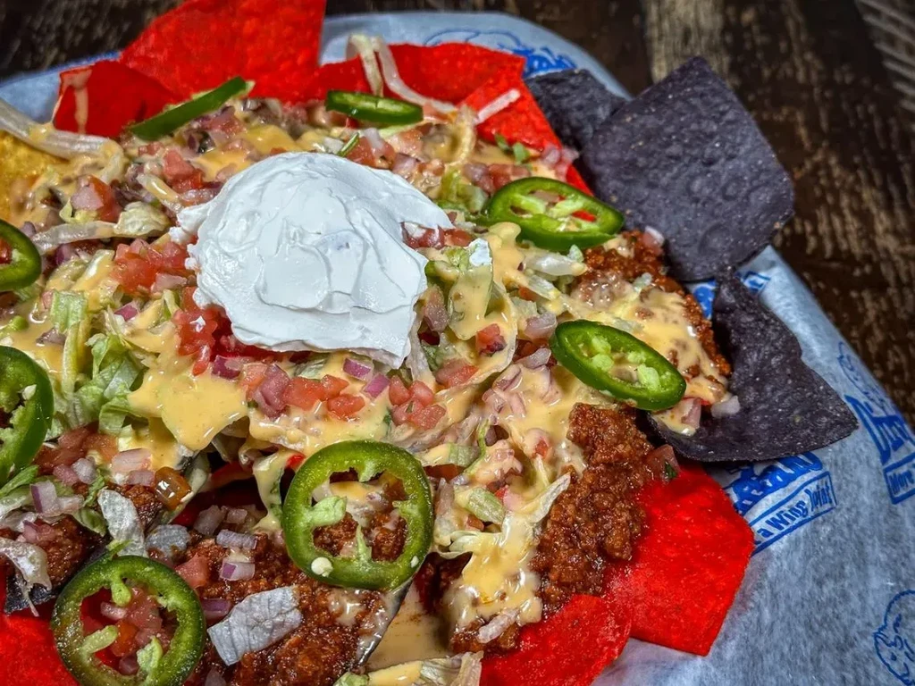Generous serving of multi-colored nachos with meat, cheese, sour cream, jalapeños.
