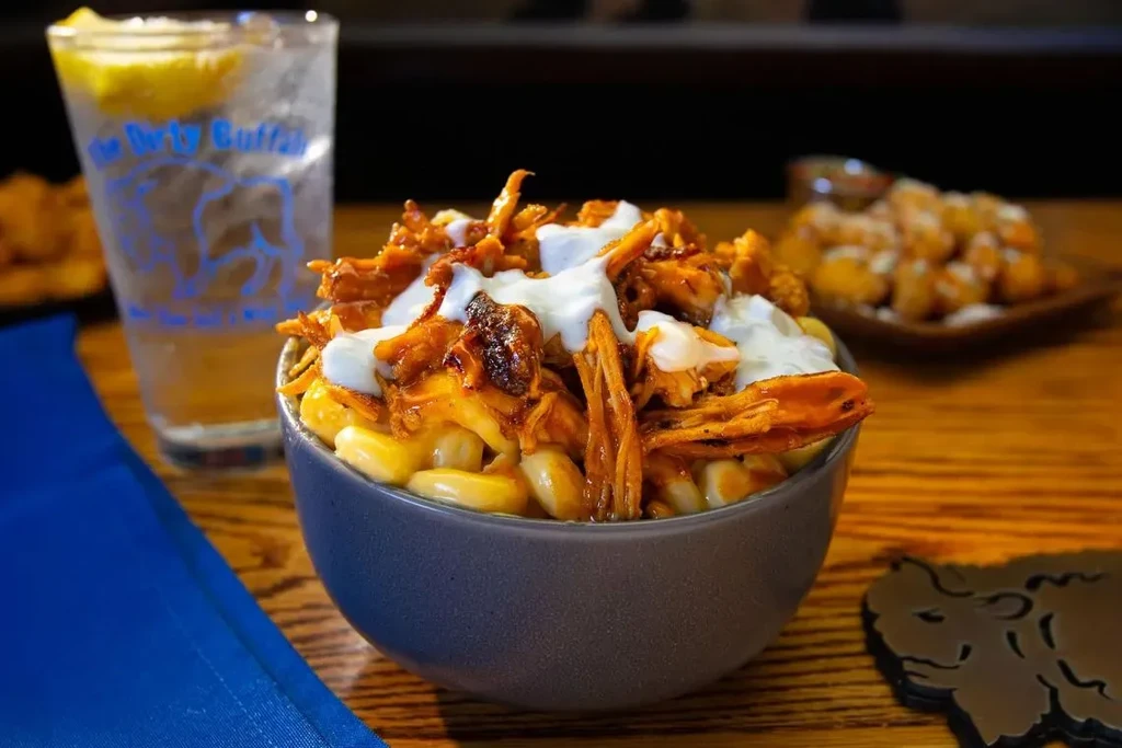 Mac and cheese topped with pulled meat, drizzled sauce, and branded glass.
