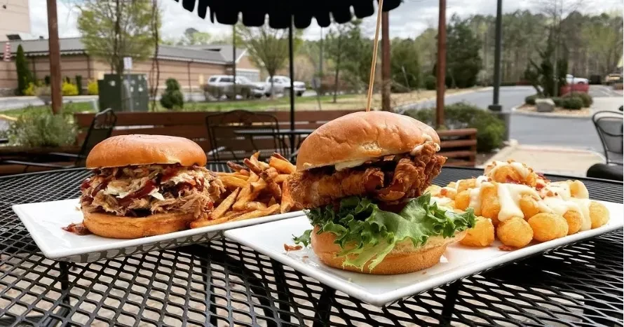 Pulled pork and fried chicken sandwiches with sides on an outdoor table.